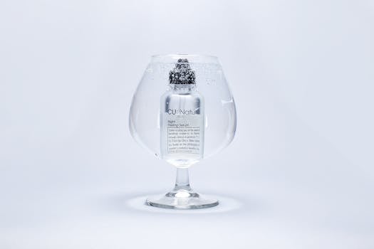 A luxury serum bottle submerged in a large wine glass filled with water, showcasing purity and elegance.