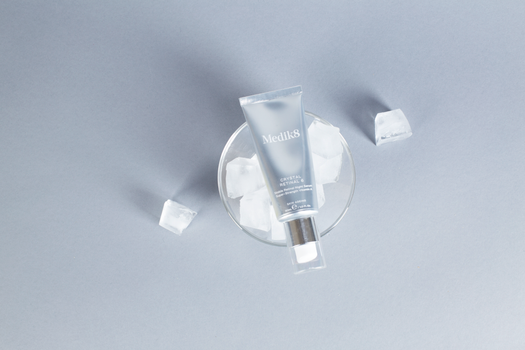 A skincare product placed on ice cubes against a gray surface for a soothing effect.