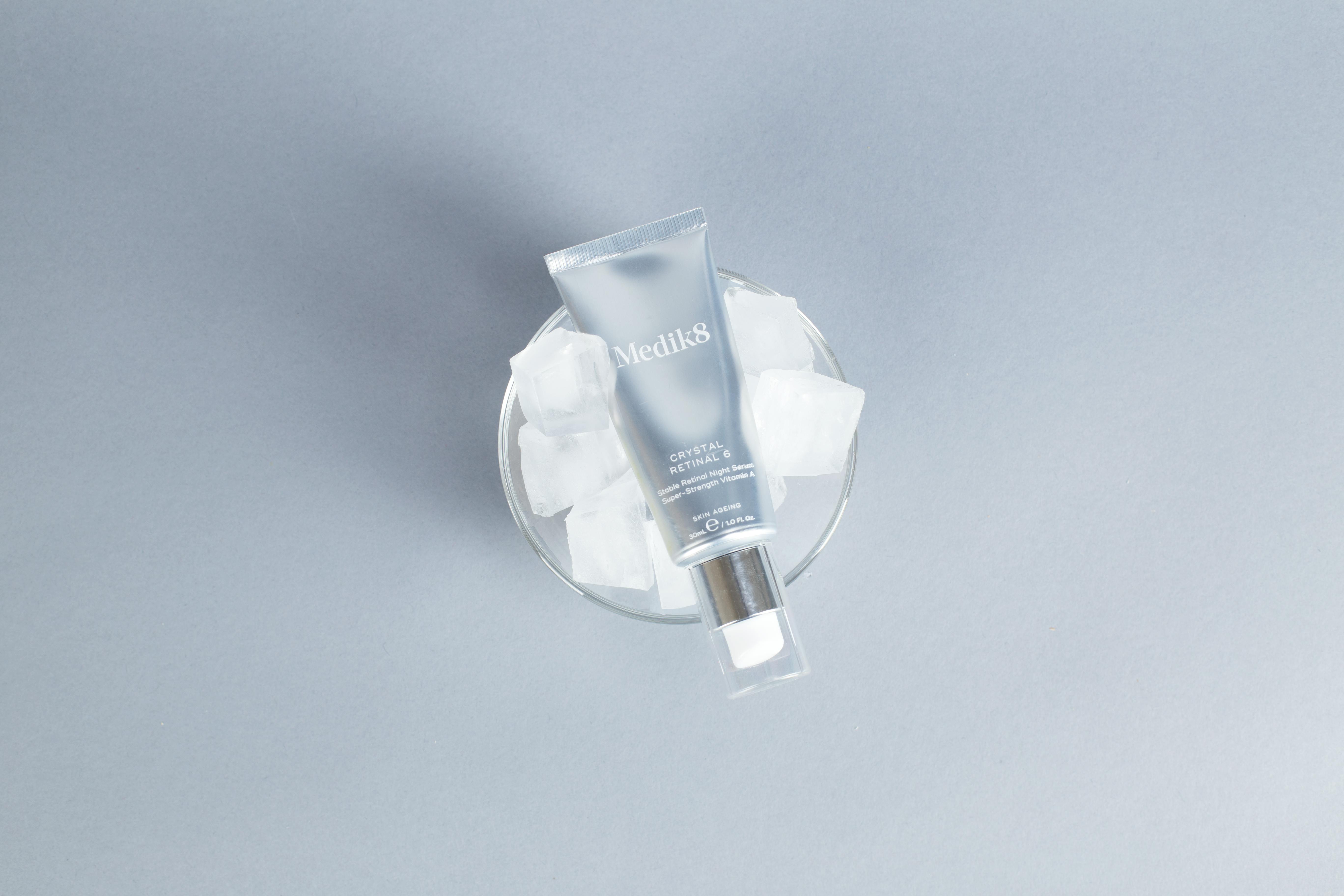 Minimalist flatlay of skincare product on ice with gray background.