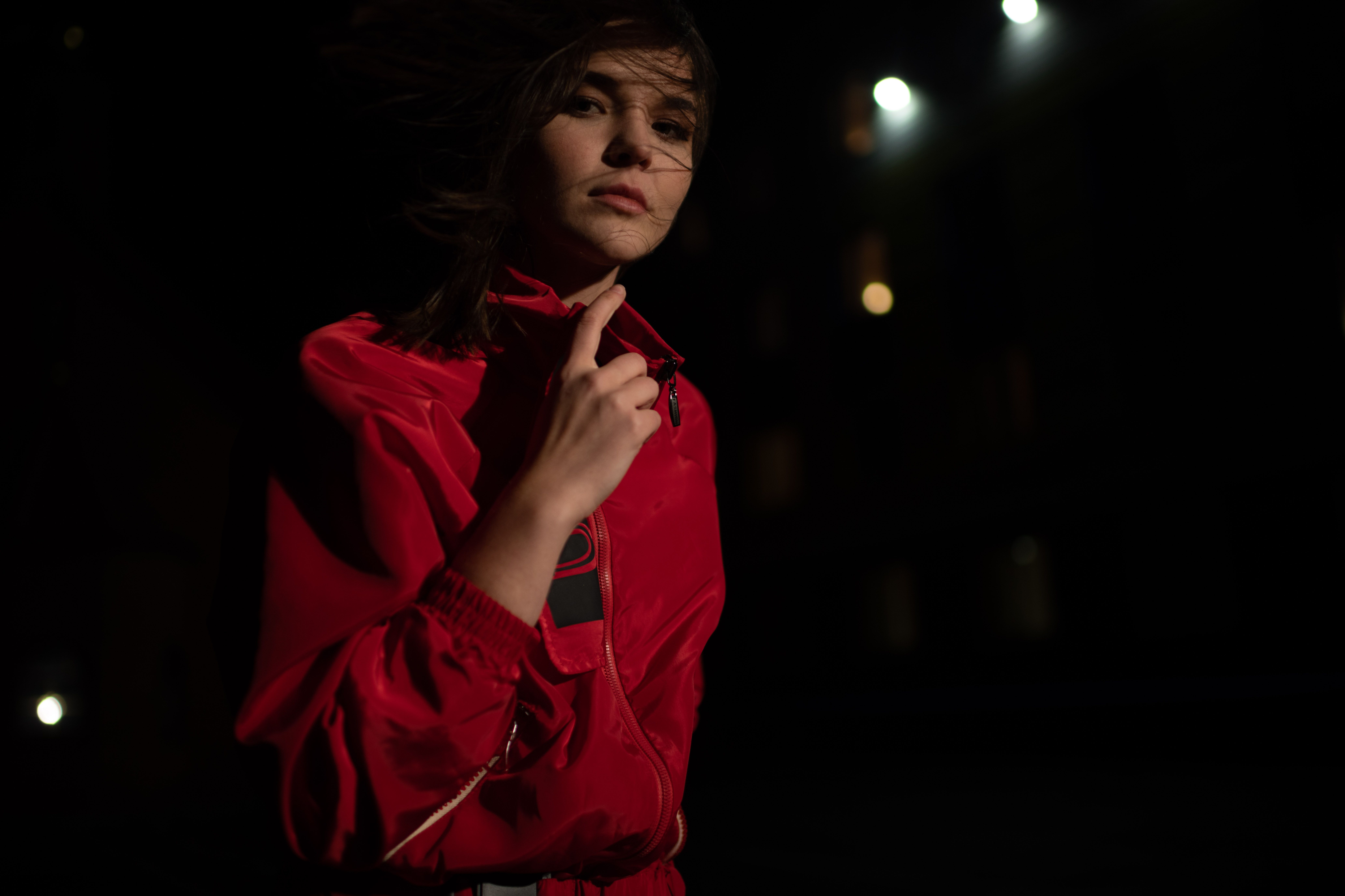 Close-up portrait of a woman in a red jacket with dynamic lighting at night.