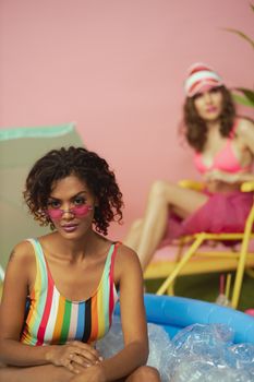 Two stylish women enjoying summer relaxation indoors with colorful accessories.