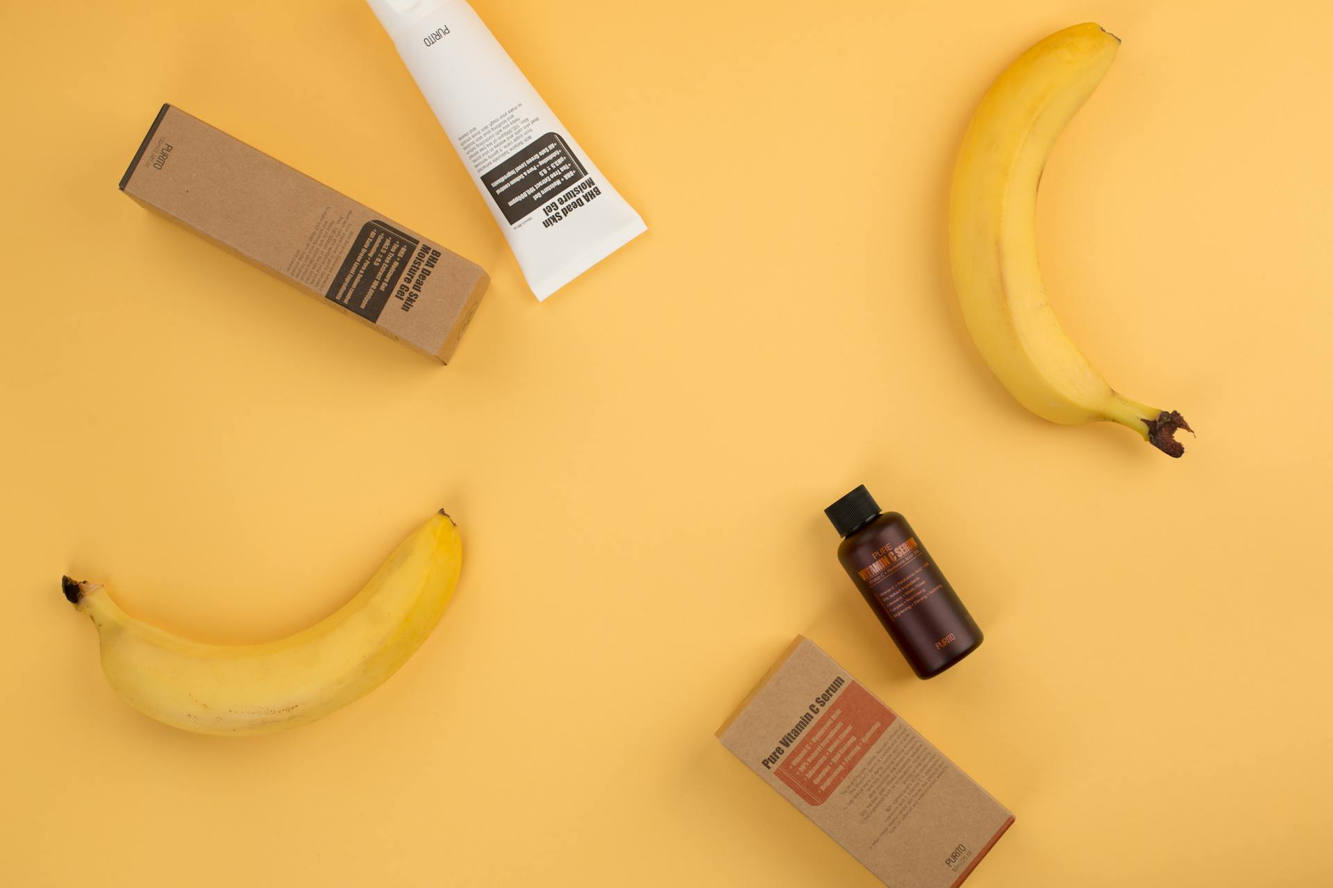 Flat lay of cosmetic products and ripe bananas against a vibrant yellow background, ideal for beauty and food concepts.