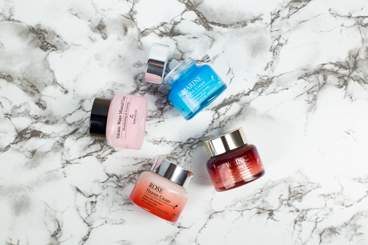 Flatlay of elegant skincare creams on marble showcasing vibrant colors and luxurious packaging.