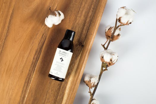 Elegant flat lay featuring treatment oil bottle and cotton on wooden surface.