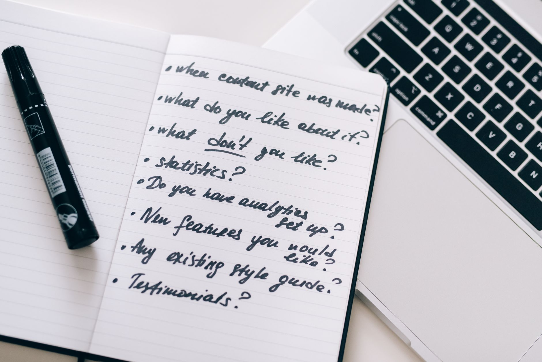 An open notebook with a handwritten list of questions next to a laptop, prepared before signing a buyer agreement