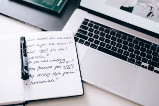 A notebook with handwritten notes next to a laptop on a workspace desk.