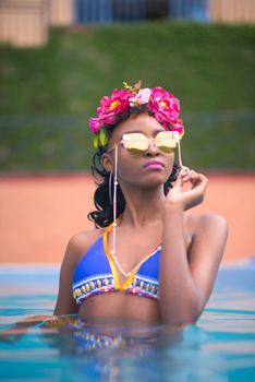 Elegant woman wearing sunglasses and floral headband enjoys a swim in the pool.