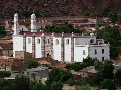 Aerial view of a historic church in Camargo, Bolivia, surrounded by lush greenery and village houses.