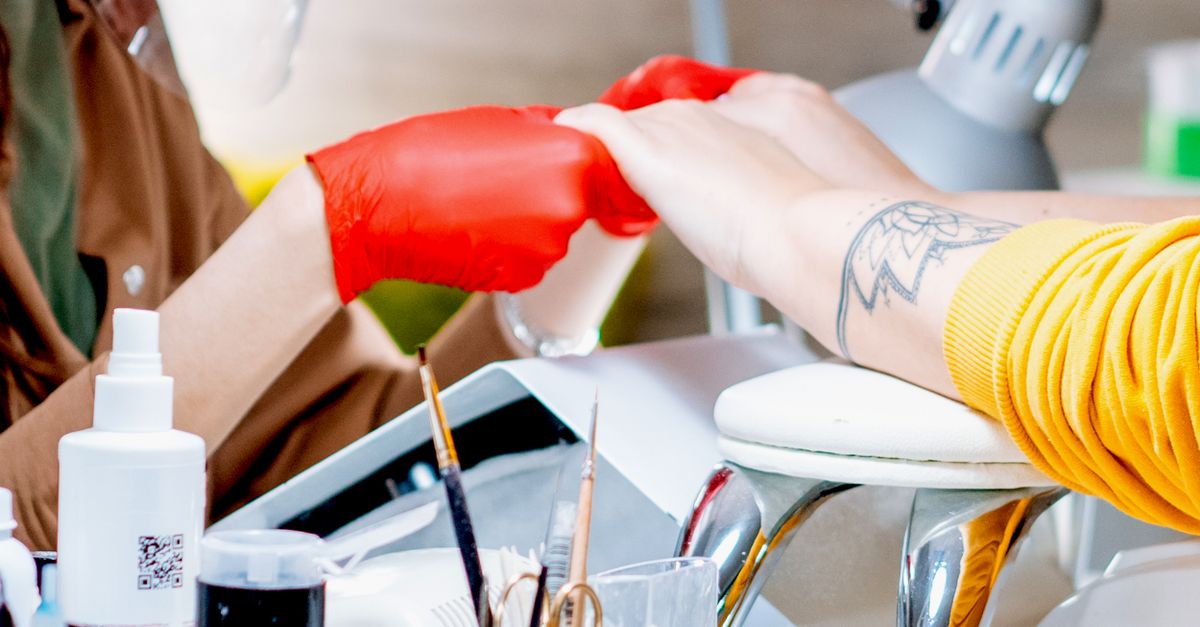 Crop anonymous master of nail salon in red gloves holding hands of unrecognizable client
