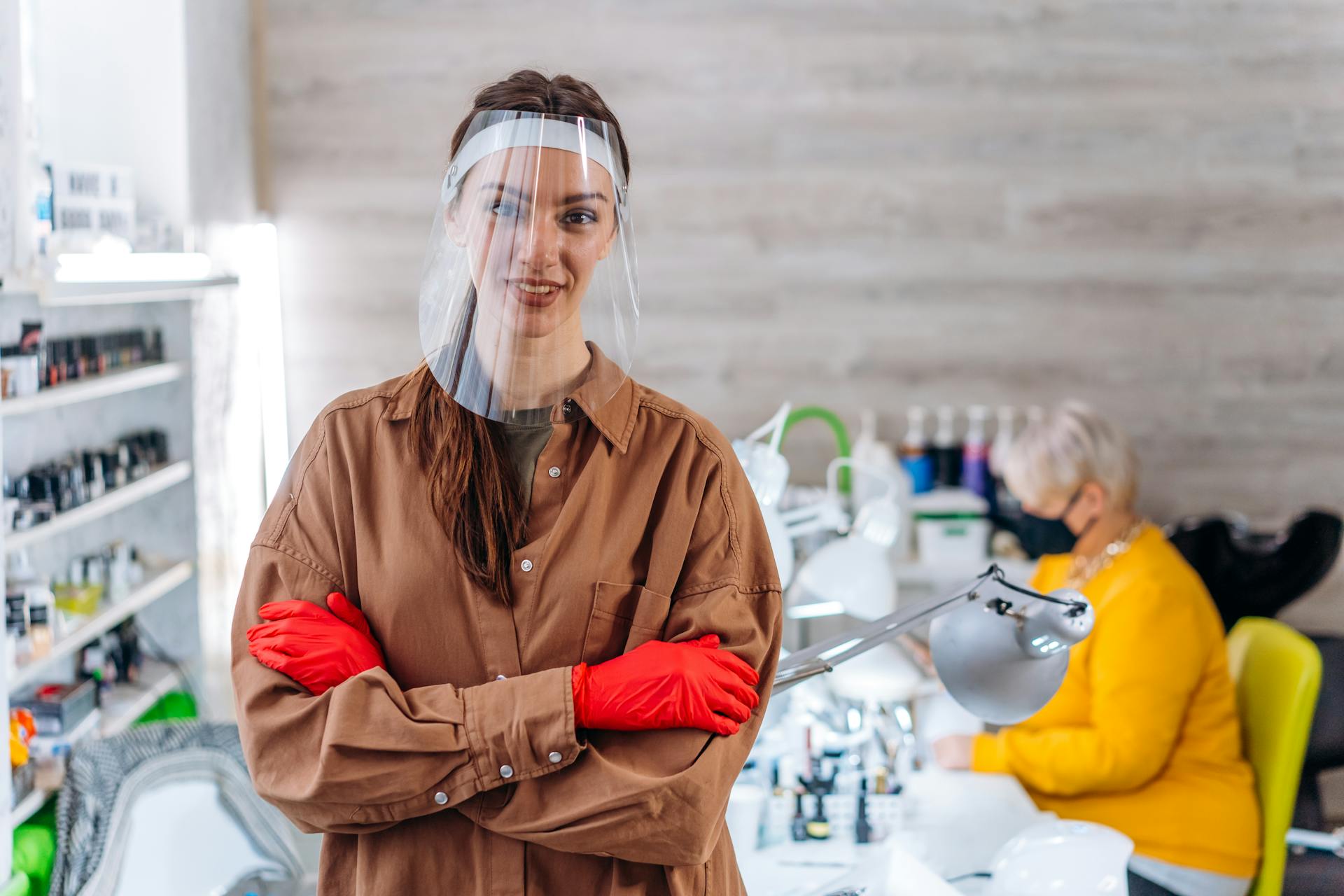 Salon worker with face shield and gloves poses indoors, embodying the new normal.