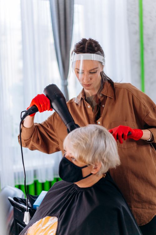 Free Hairdresser using face shield and mask while styling client indoors during pandemic. Stock Photo