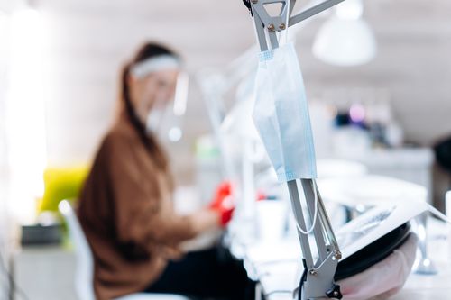 Free Focus on a face mask hanging in a blurred office with a person working, symbolizing the new normal. Stock Photo