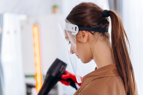 Free A hairdresser wearing a face shield uses a blow dryer in a salon, embracing safety measures. Stock Photo