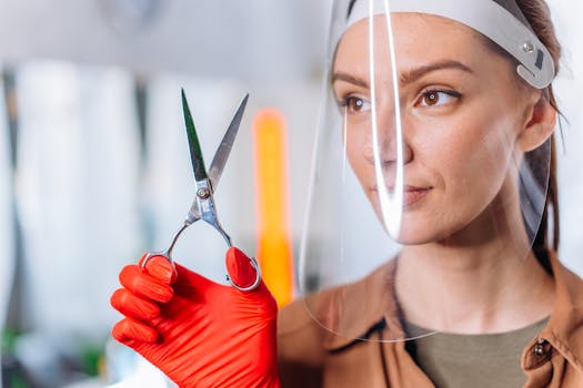 Hairdresser wearing a face shield holding scissors in a salon, showcasing the new normal.