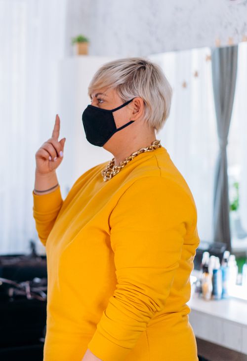 Free Side view of a stylish woman with gray short hair wearing a mask and yellow sweater indoors. Stock Photo