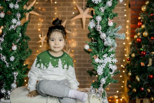 Photo of a Girl in a Green and White Sweater Sitting Near Garlands