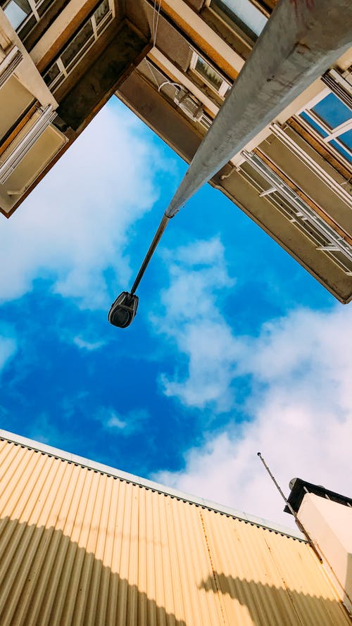 Free From below of streetlight pole placed near tall residential houses against blue sky with clouds on sunny summer day in city Stock Photo