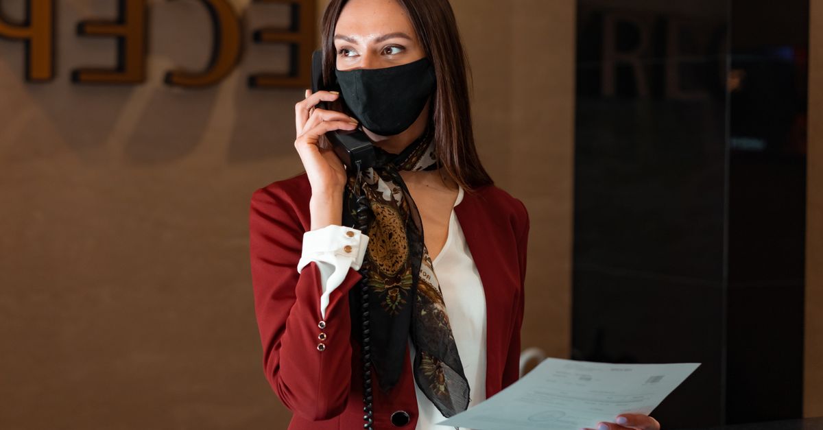 A female receptionist with a face mask answers a phone call, embodying professional service and safety.
