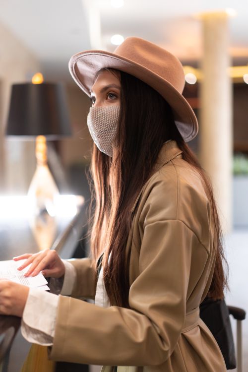 Free Stylish woman with long hair, wearing a beige coat and fedora, in an indoor setting. Stock Photo