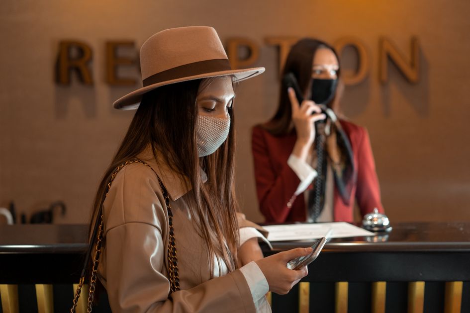 Woman wearing a mask checking her phone at a hotel reception during COVID-19. Related image for AI in hospitality in Canada hotels.