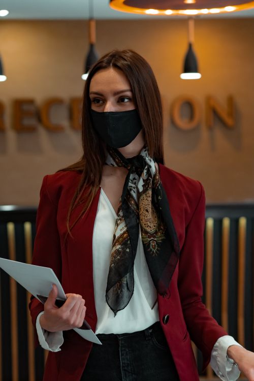 Free Professional woman in hotel reception wearing mask and red blazer, creating a modern stylish look. Stock Photo