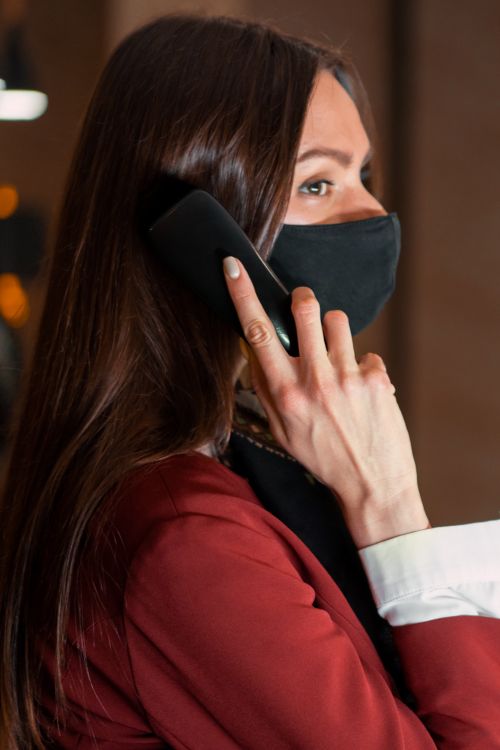 Free Woman wearing a mask using a phone at a hotel reception desk, embracing the new normal. Stock Photo
