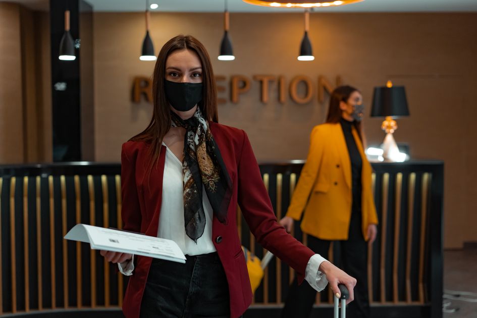 A woman in a mask stands at a hotel reception desk holding paper, welcoming service Related image for AI in hospitality in Global hotels.