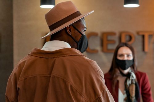 Free A masked tourist with a hat checks in at a hotel reception, practicing new normal protocols. Stock Photo