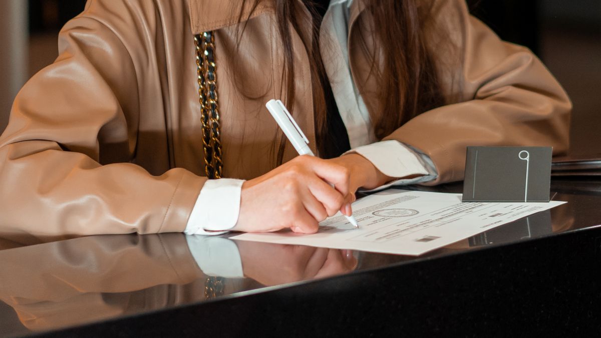 Close-up of a woman signing a document at a sleek reception counter, indoor setting.