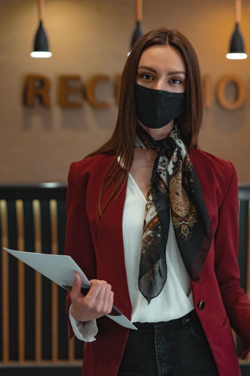 Free Woman wearing a face mask and red blazer holding documents at a reception desk. Stock Photo