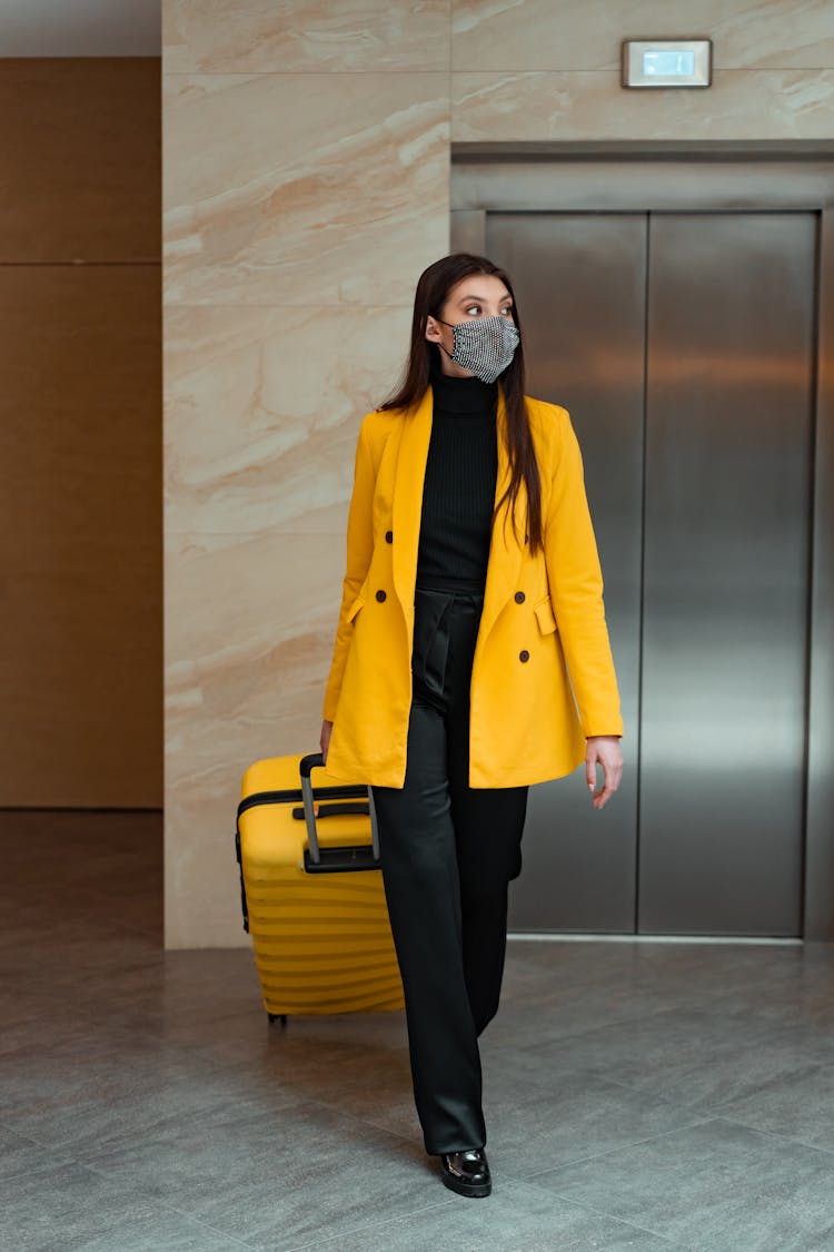 A Woman In Yellow Coat Walking While Holding Her Luggage