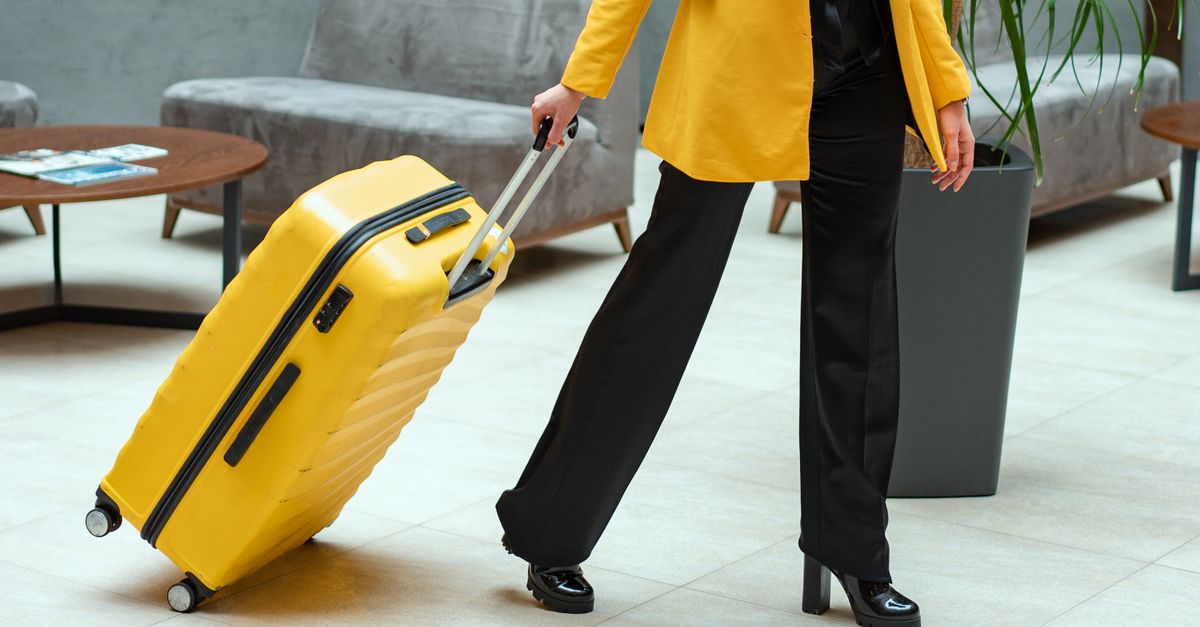 Mulher estilosa caminhando no lobby do hotel puxando uma mala amarelo brilhante.