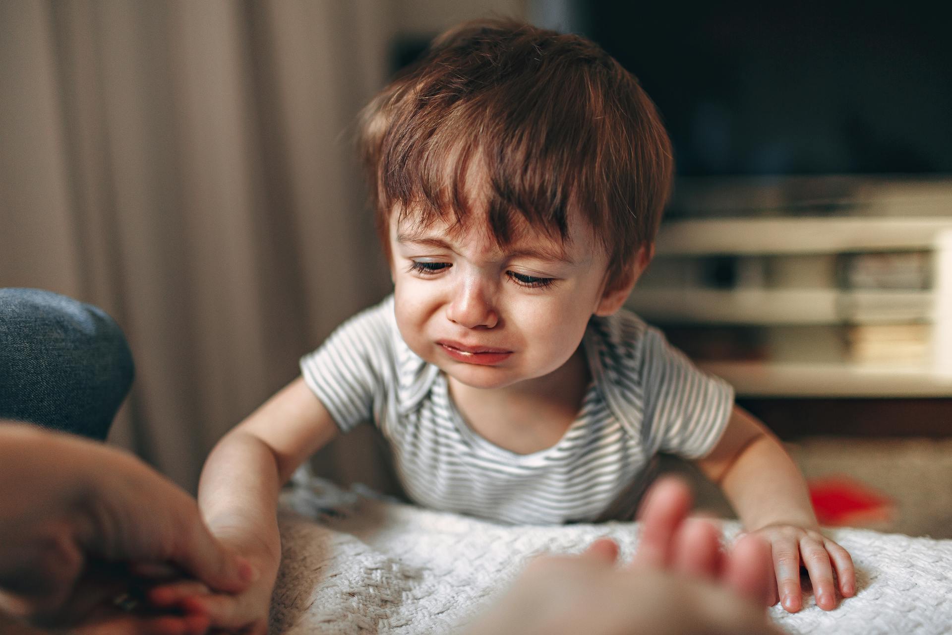 A close-up of a crying child indoors, displaying strong emotions and frustration.