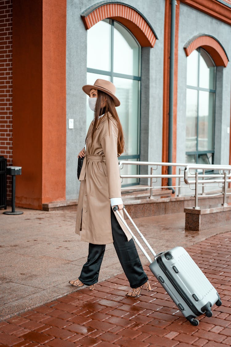 Photo Of A Woman In A Brown Coat Walking With Her Gray Suitcase