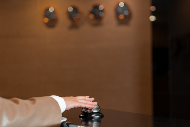 A hand pressing a bell at a hotel reception, symbolizing service and hospitality. Related image for AI in Hospitality: What Hotel Leaders Need to Know.
