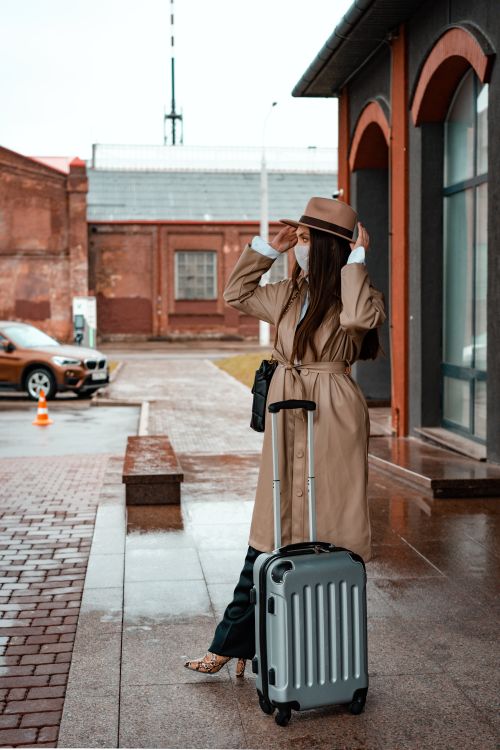 Free Elegant woman in a trench coat, waiting outside with a suitcase, embracing travel. Stock Photo