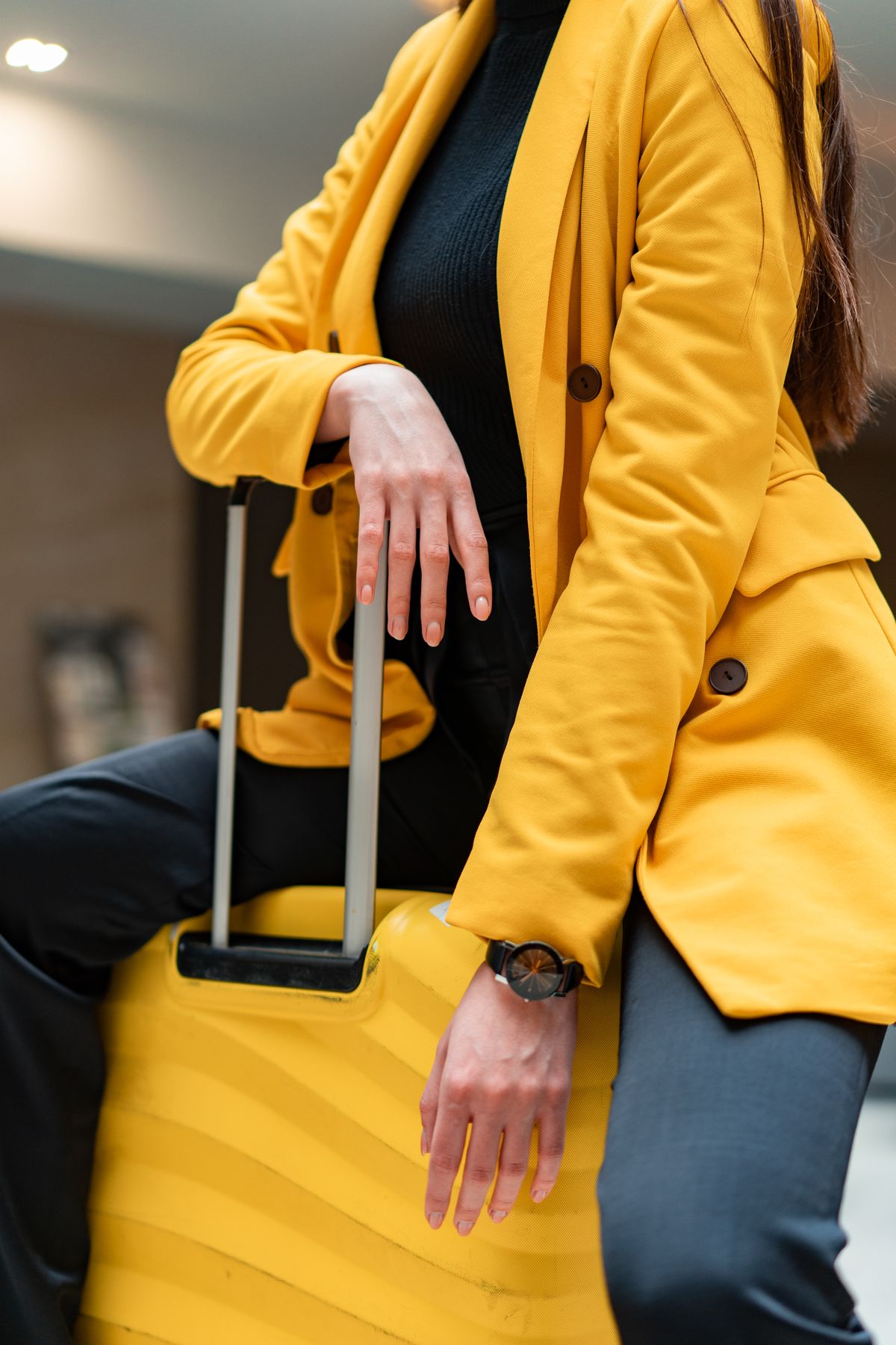 Woman in a bright yellow coat sitting on yellow luggage at an airport