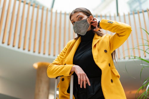 Low-Angle Shot of a Woman in a Yellow Coat Wearing a Face Mask