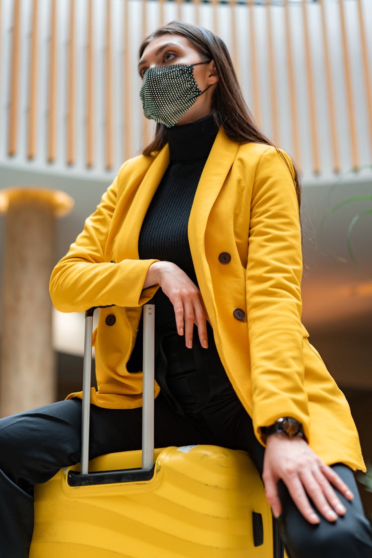 Low-Angle Shot Of A Woman In A Yellow Coat Sitting On A Luggage Bag