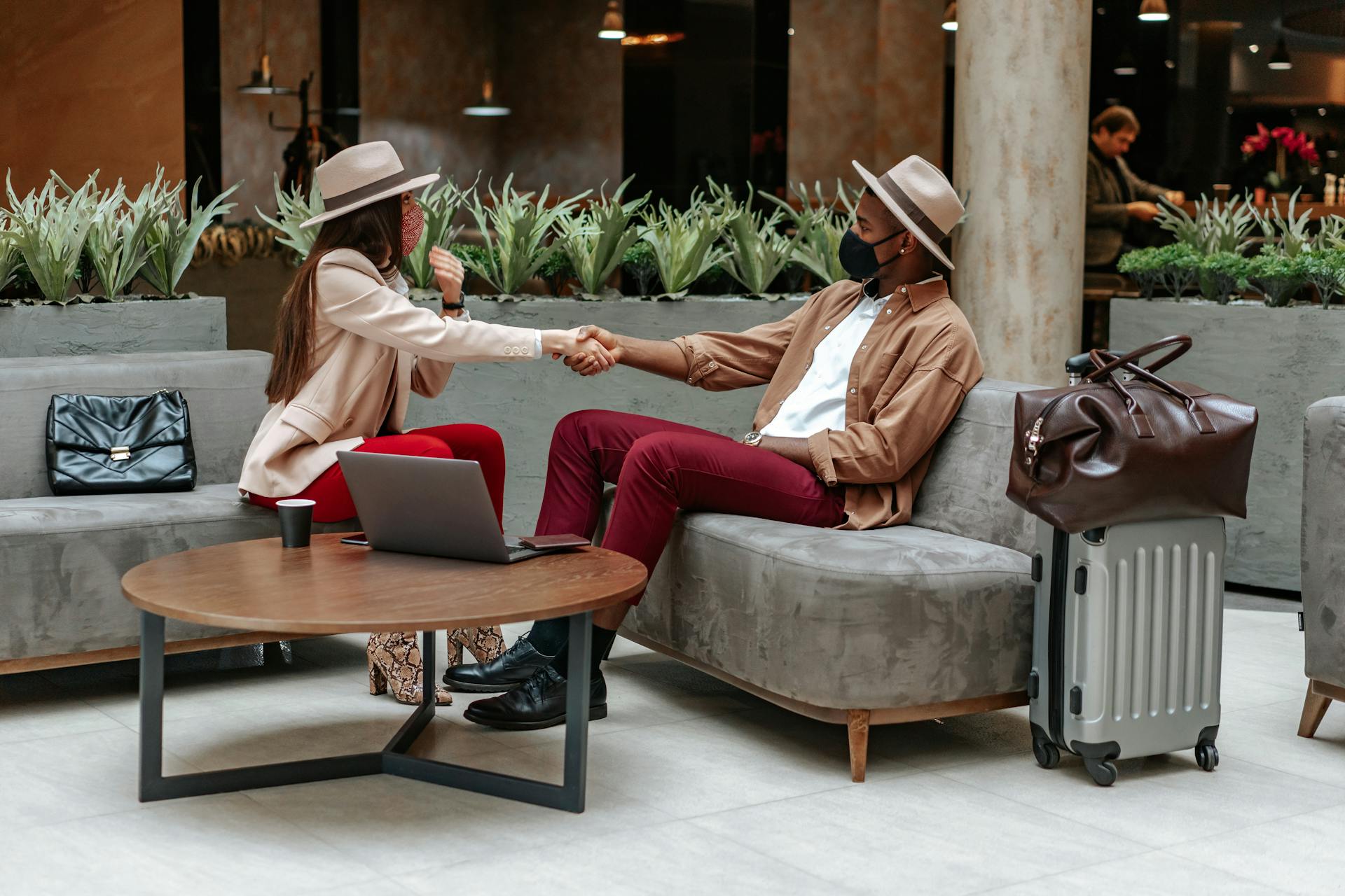 Two fashionable individuals shaking hands in a hotel lobby, showcasing travel and safety.