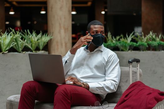 Professional man multitasks with laptop and smartphone in a modern indoor sitting area.