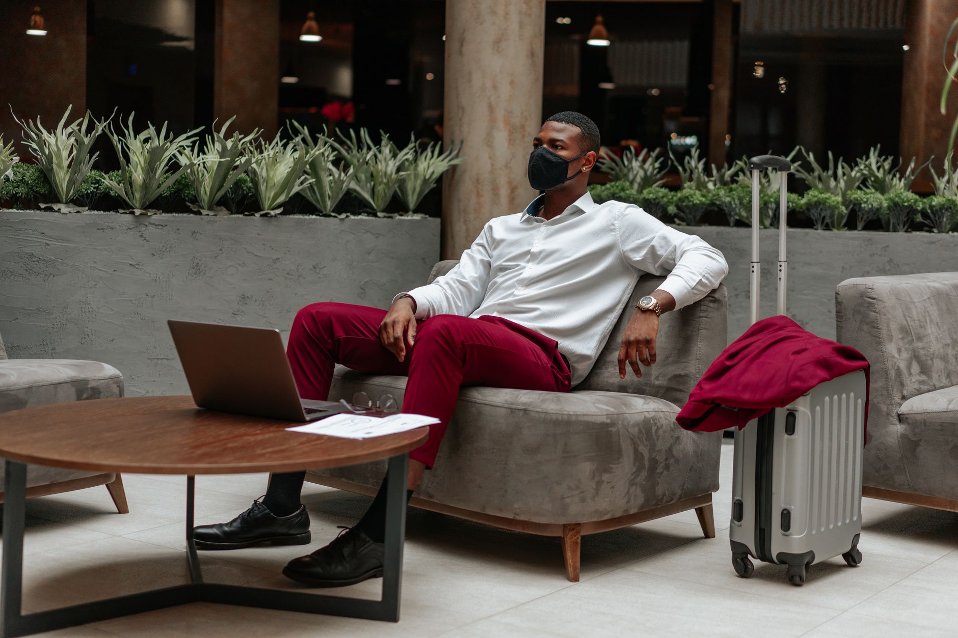 Man wearing facemask, sitting in hotel lobby with laptop and suitcase, adapting to new normal. Related image for Hotel Technology: How Operators Are Using Better Data.