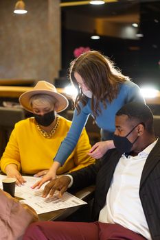 Three people collaborate safely with masks during a meeting indoors.