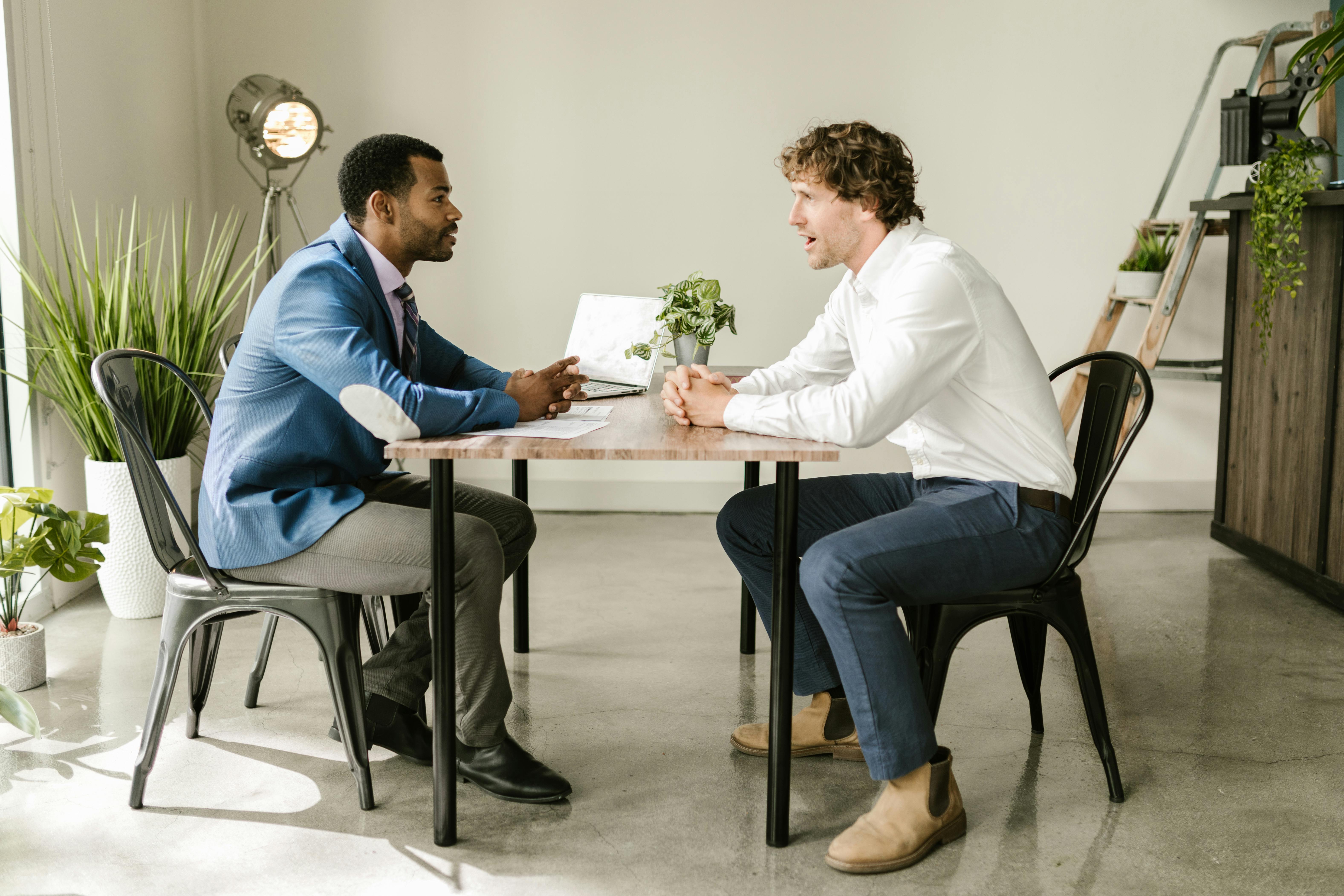 Free Two businessmen engaged in a professional discussion at an indoor office setting with greenery and modern decor. Stock Photo