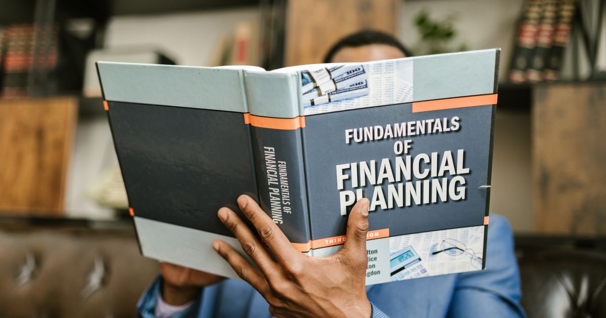 A professional individual in a suit reading 'Fundamentals of Financial Planning' indoors.