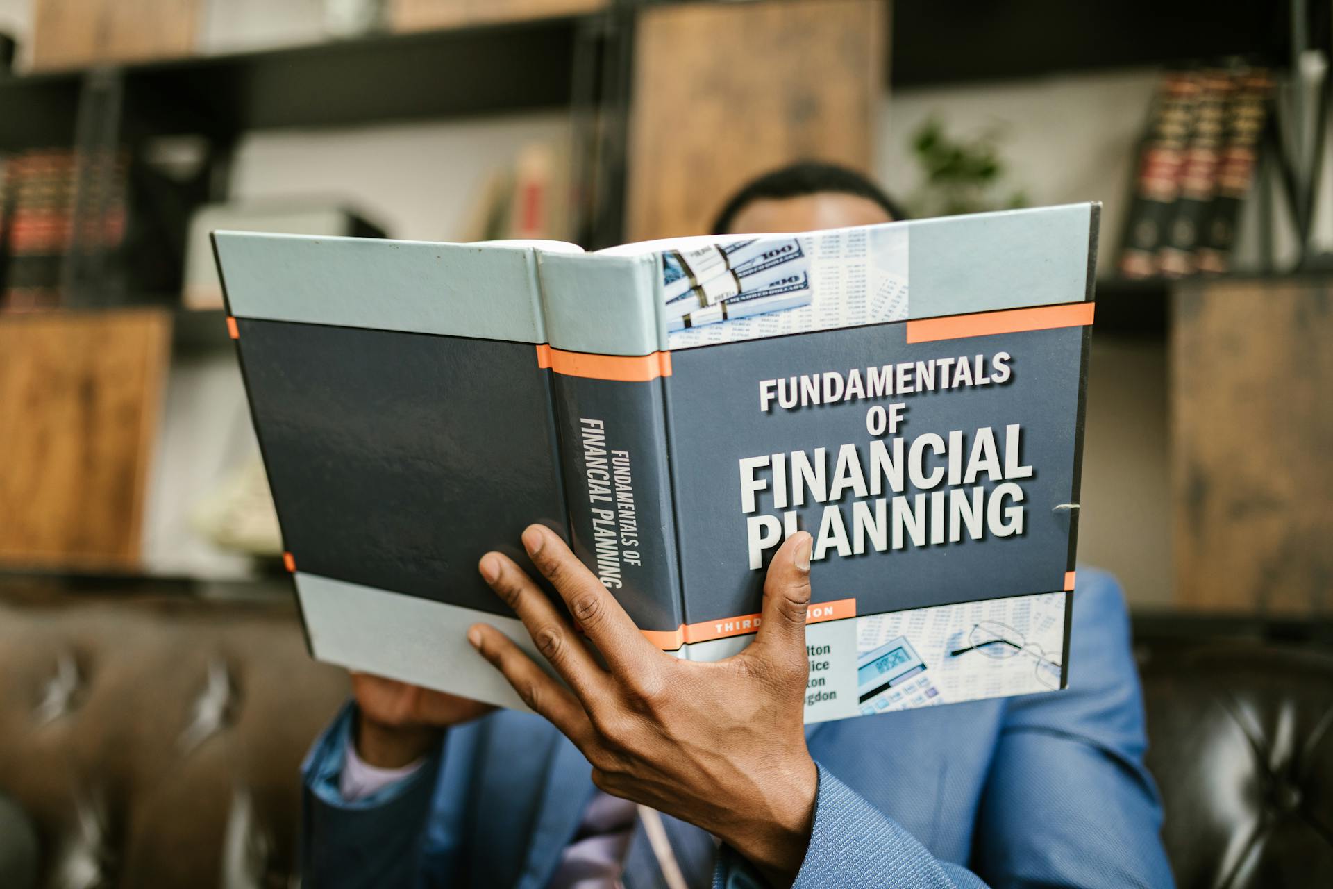 A professional individual in a suit reading 'Fundamentals of Financial Planning' indoors.