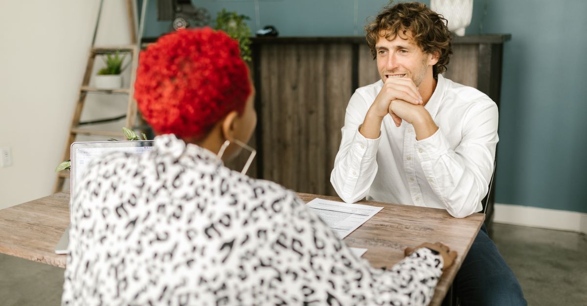 Two adults engaging in a relaxed office conversation across a desk.