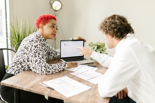 Free Colleagues discussing work over a laptop in an office setting, pointing to the screen. Stock Photo