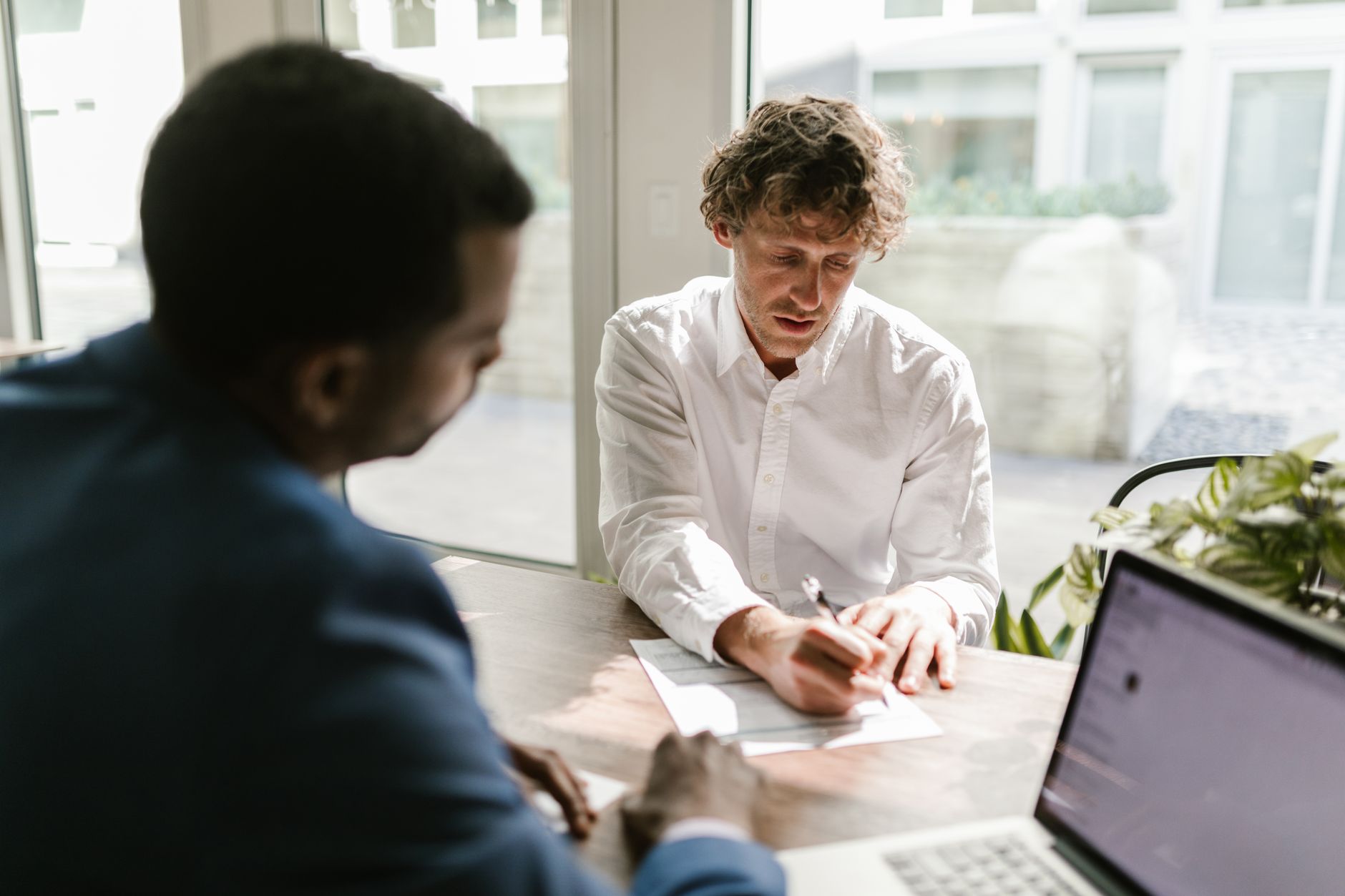 Two professionals at a desk with a laptop, reviewing a printed agreement together