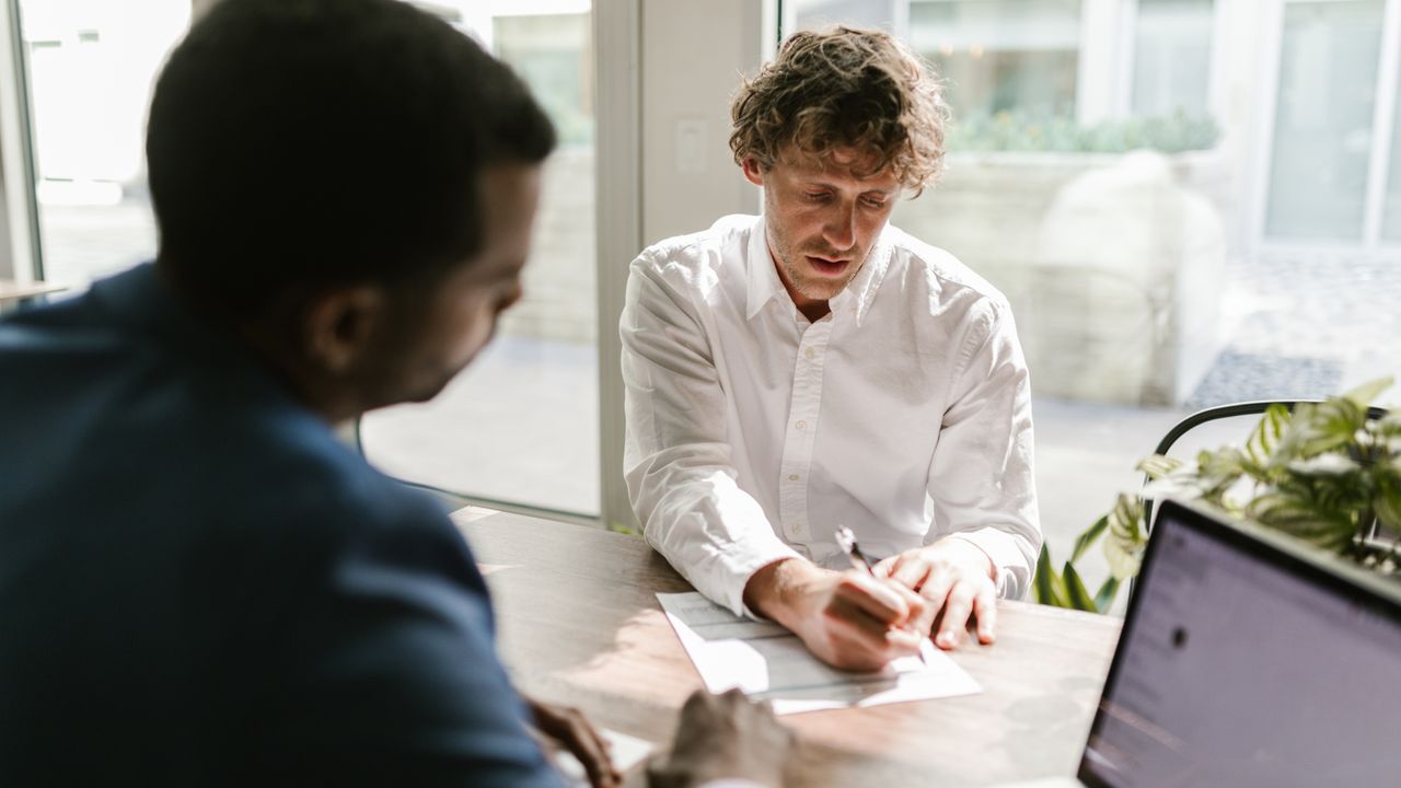 Two men collaborating in a modern office, reviewing and signing documents.